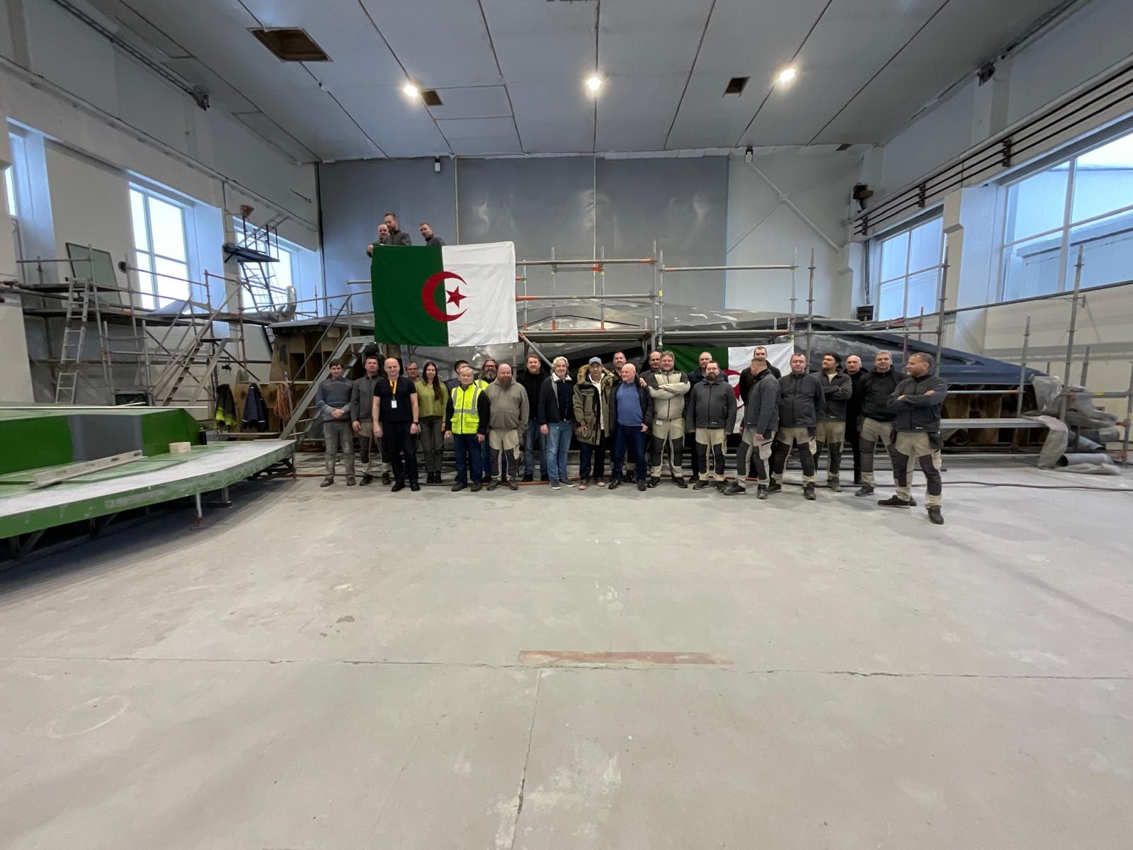 L’équipe du chantier en Algérie devant une coque en construction, drapeau algérien déployé